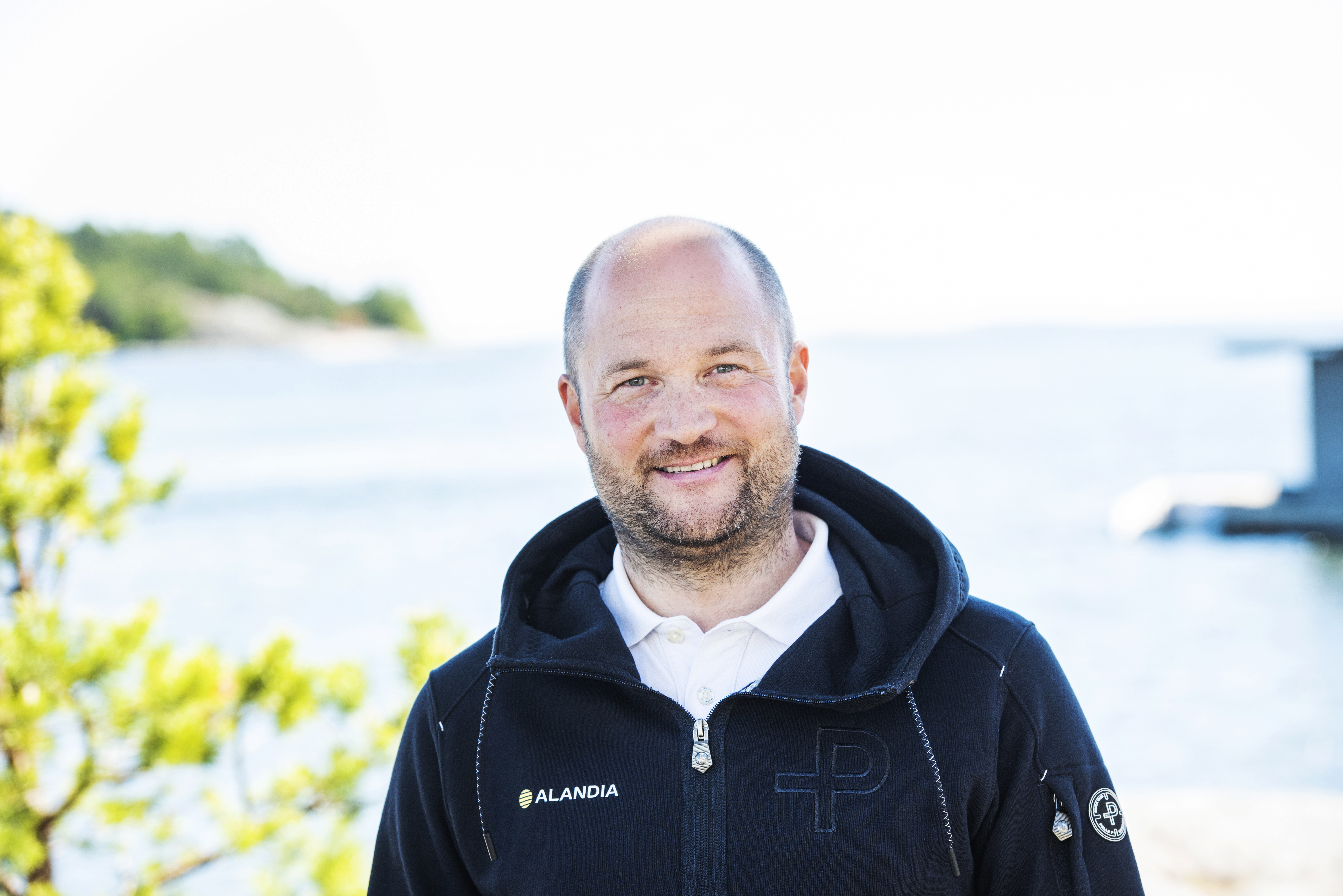Man tittar leende in i kameran. I bakgrunden syns ett havslandskap.