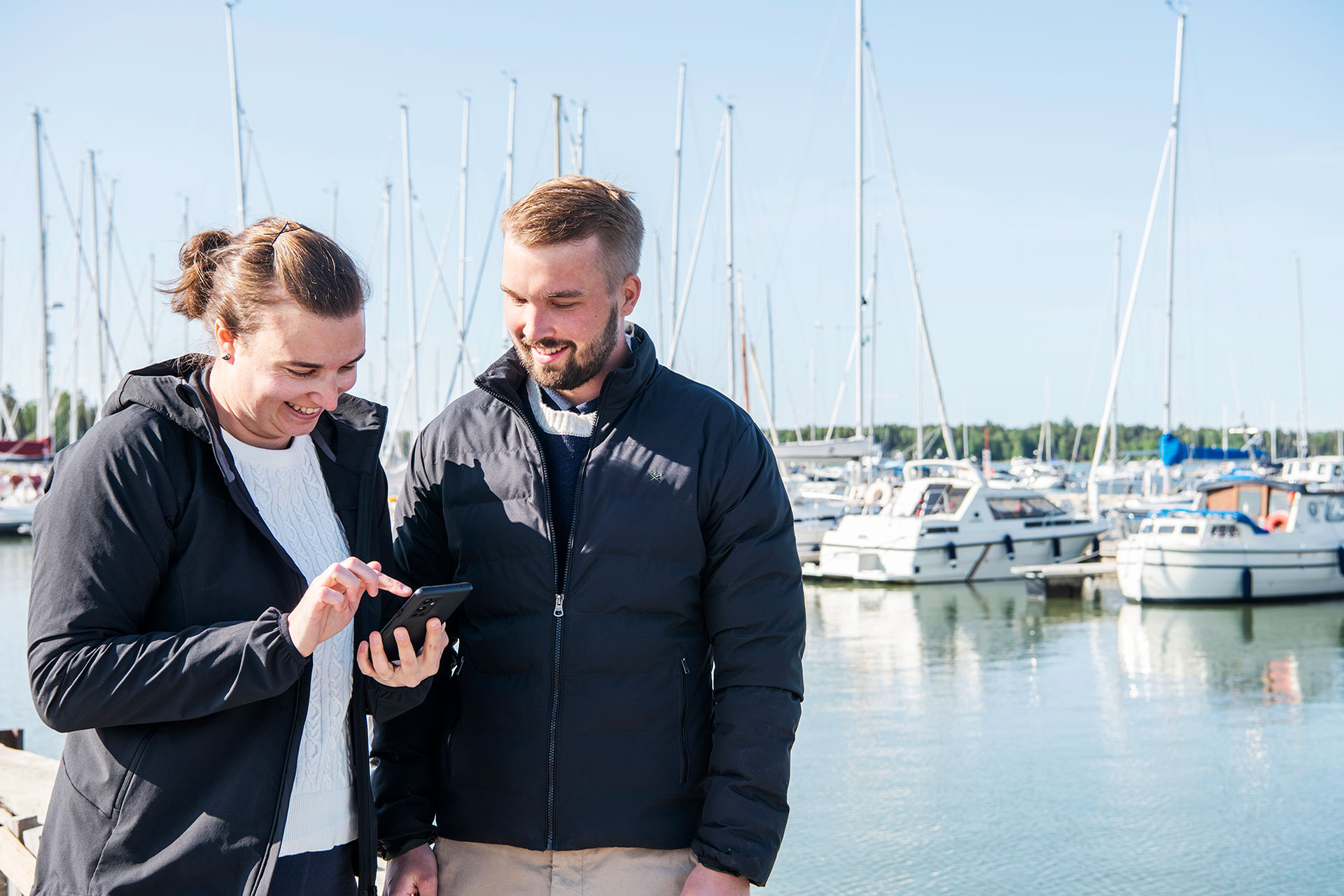 En kvinna och en man tittar på en telefon i en småbåtshamn.
