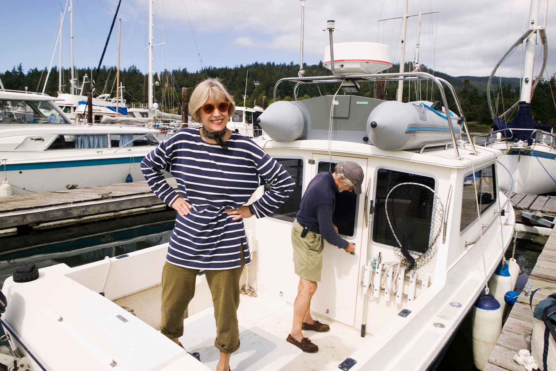 A woman and a man standing in a motorboat at harbour. The man os locking the door of the cabin.