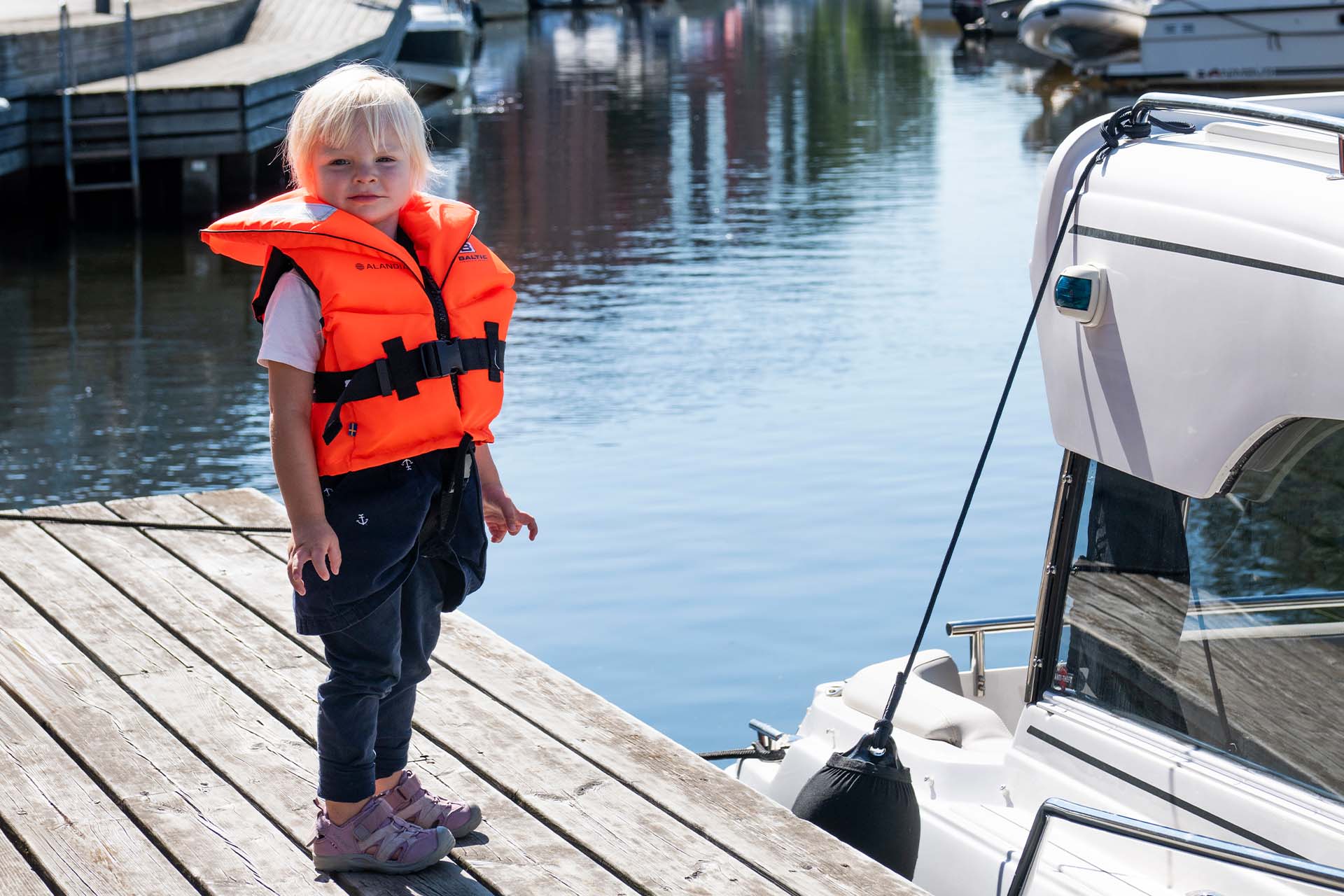 Ett litet barn står på bryggan med räddningsväst på sig.