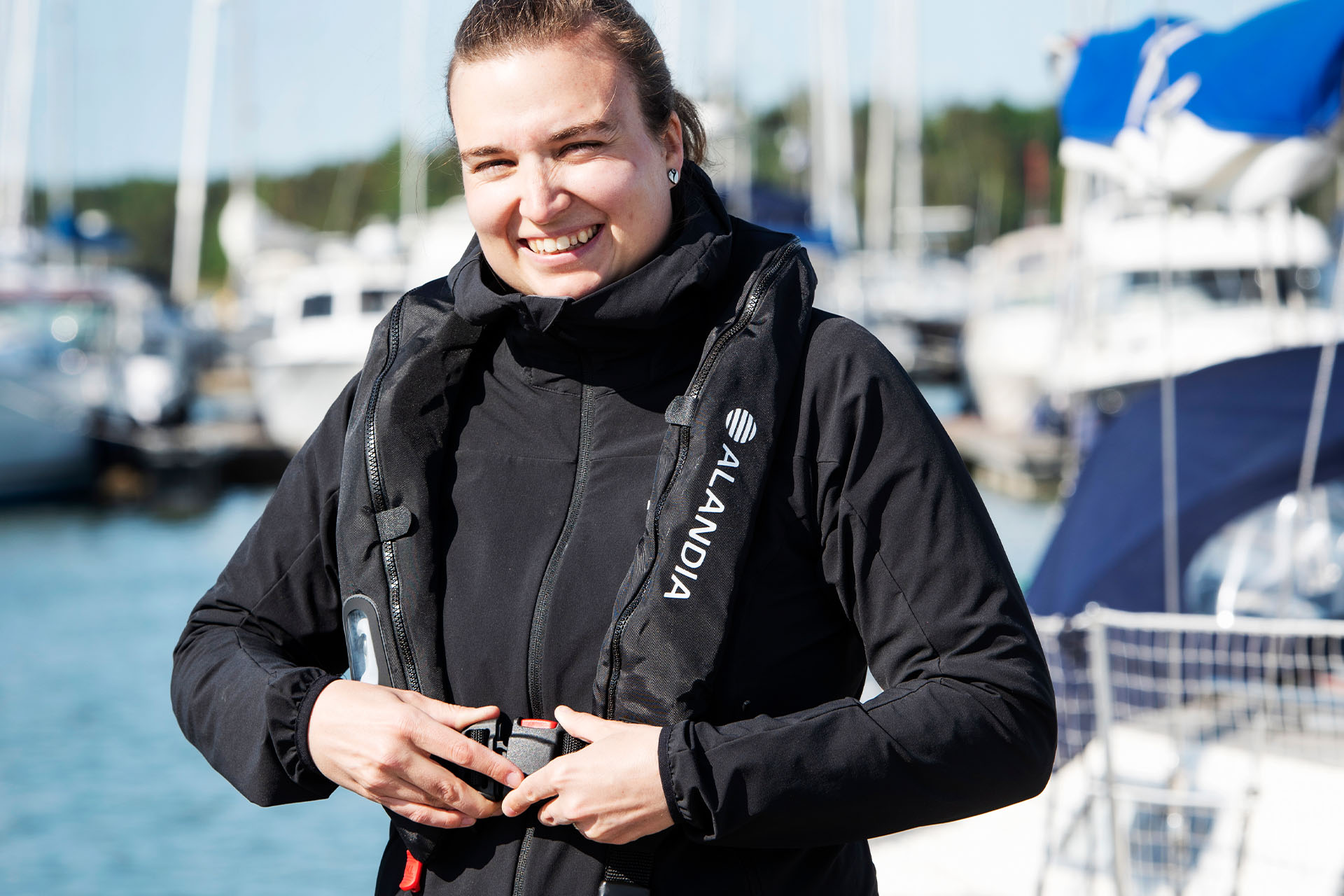 En kvinna står leende på bryggan och knäpper sin uppblåsbara räddningsväst.